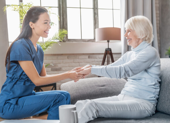 Assisting senior people. Female caregiver holding elderly woman's hands indoors