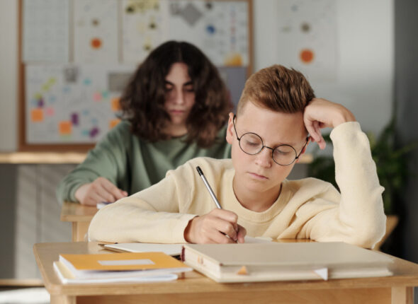 Clever youthful schoolboy making notes in copybook during individual assignment