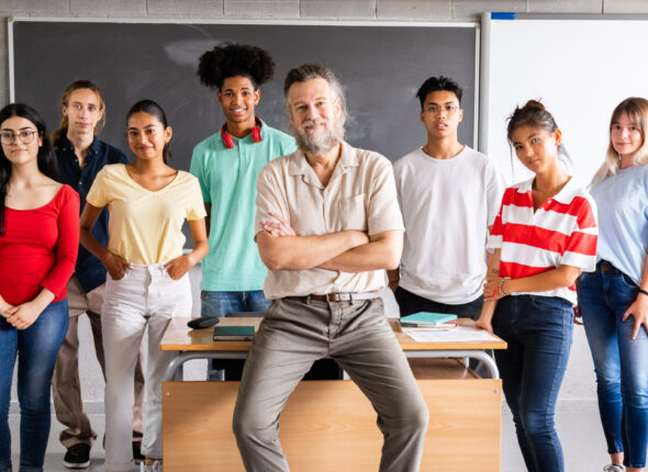 Mature male high school teacher with his multiracial group of teen students looking at camera. Horizontal banner image.