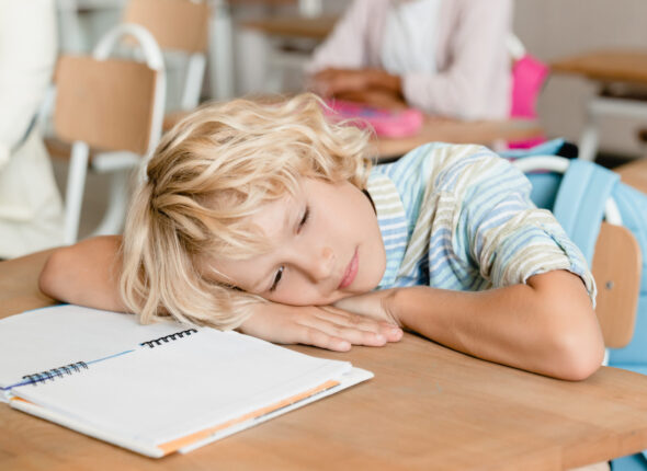 Sleepy tired bored schoolboy pupil student sleeping at the desk in school during the lesson class.